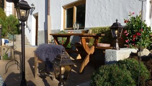 An outdoor patio with a wooden table and chairs, a lamp post, and a small garden area with plants and flowers. - Appartement Aschbach (Kitzbuhel)