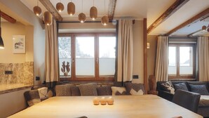 A spacious dining area with a long wooden table, multiple chairs, and a cozy seating arrangement with cushions. - Appartement Aschbach (Kitzbuhel)