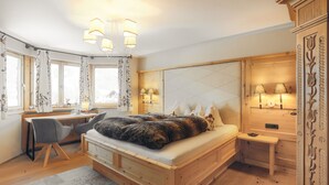 A cozy bedroom with a wooden bed, a desk with a chair, and a bedside table with lamps. - Appartement Aschbach (Kitzbuhel)