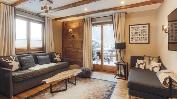 A cozy living room with a sofa, a bench, and a bed. There is a fireplace, a window, and a wall with framed pictures. - Appartement Aschbach (Kitzbuhel)