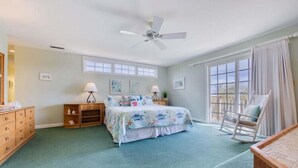 A bedroom with a bed, a rocking chair, a dresser, a nightstand, and a ceiling fan. - Chapman - 2 Blocks to Beach Access - Resort Amenities (Duck)