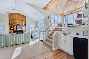 A spacious living area with a large sofa, a wooden ceiling, and a kitchen with white cabinets. - Chapman - 2 Blocks to Beach Access - Resort Amenities (Duck)