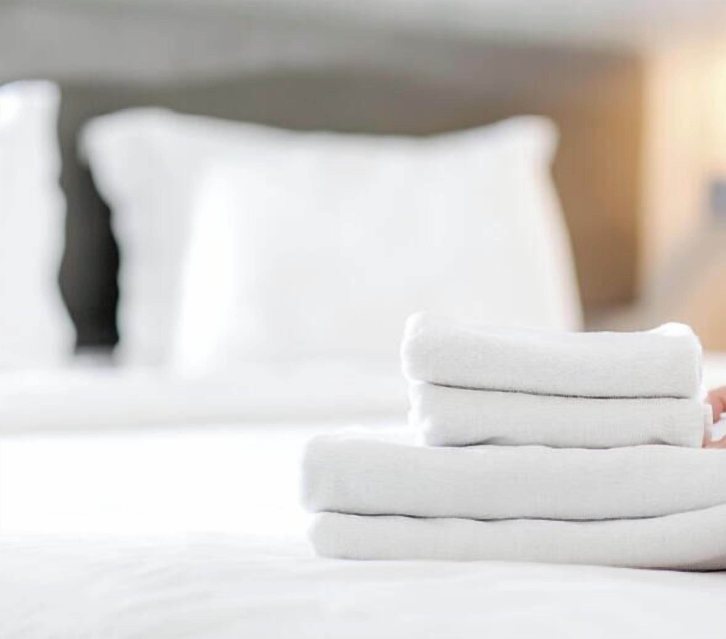 A person folding a stack of white towels on a bed.