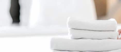 A person folding a stack of white towels on a bed.