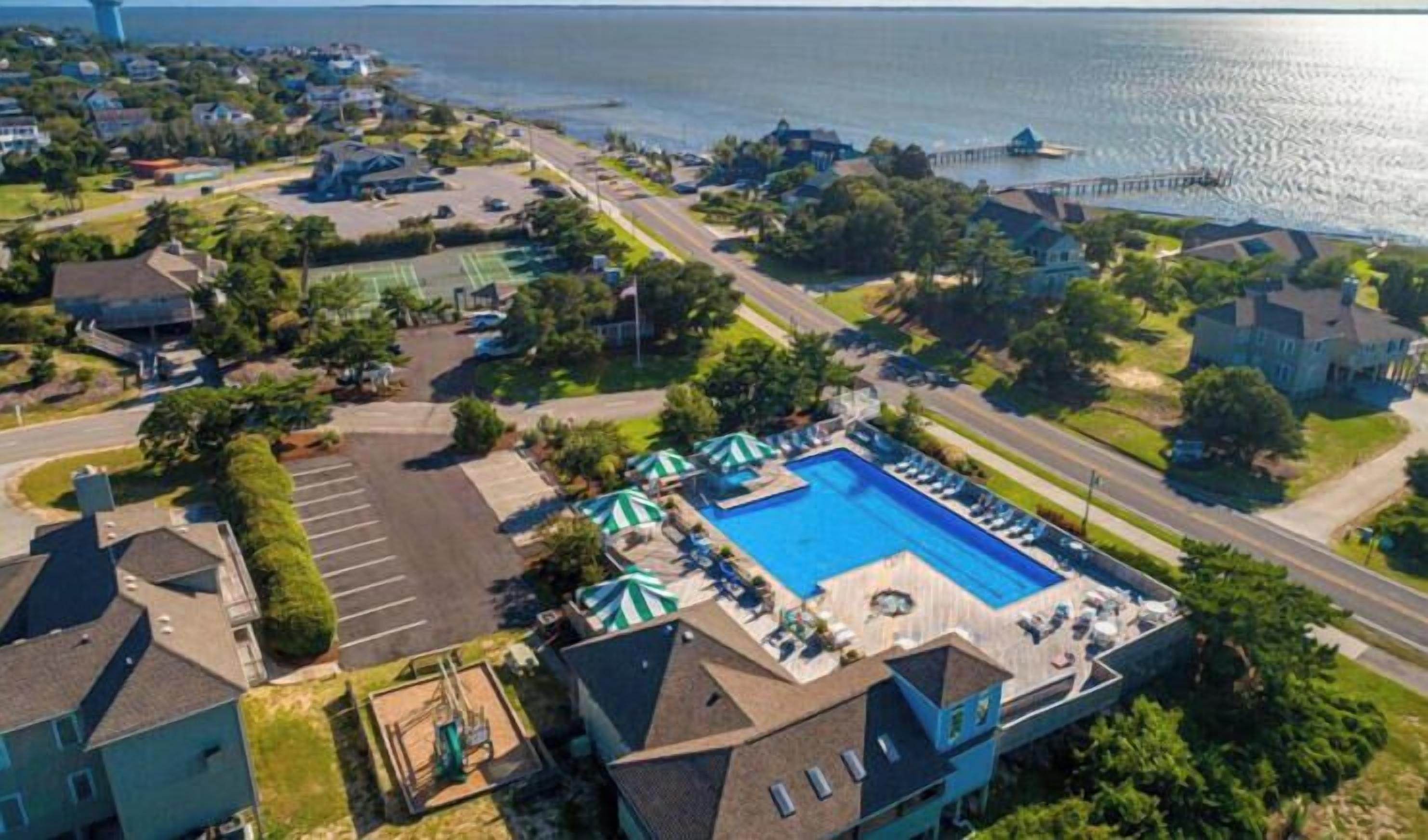 An aerial view of a residential area with a swimming pool, tennis courts, and a waterfront.