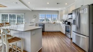 A modern kitchen with a central island, stainless steel appliances, and a view to the outside. - LITTLE is only 1 block walk to beach access - 4 BR - sleeps 8 (Duck)