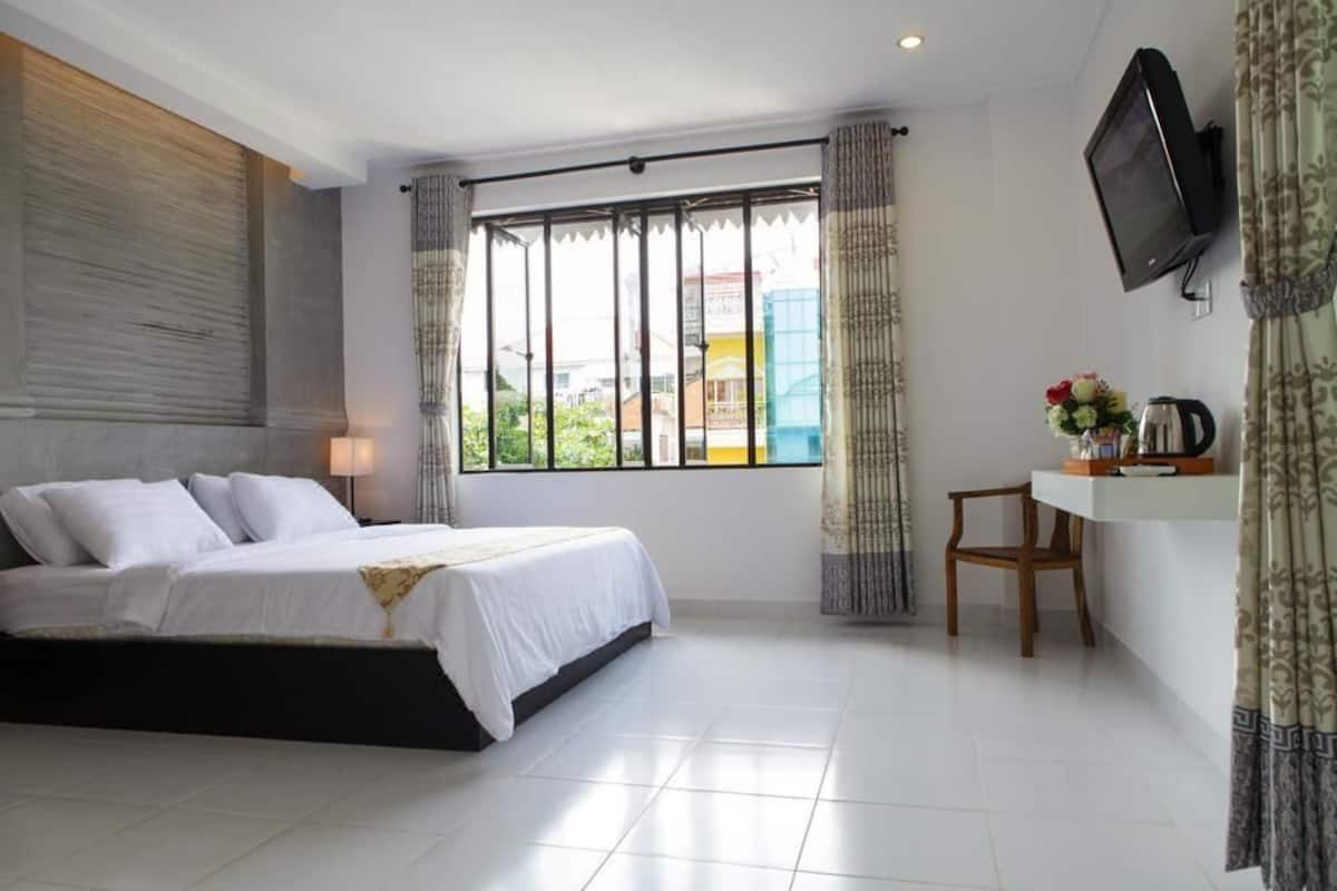 A bedroom with a bed, a TV, a desk with a chair, and a window with curtains.