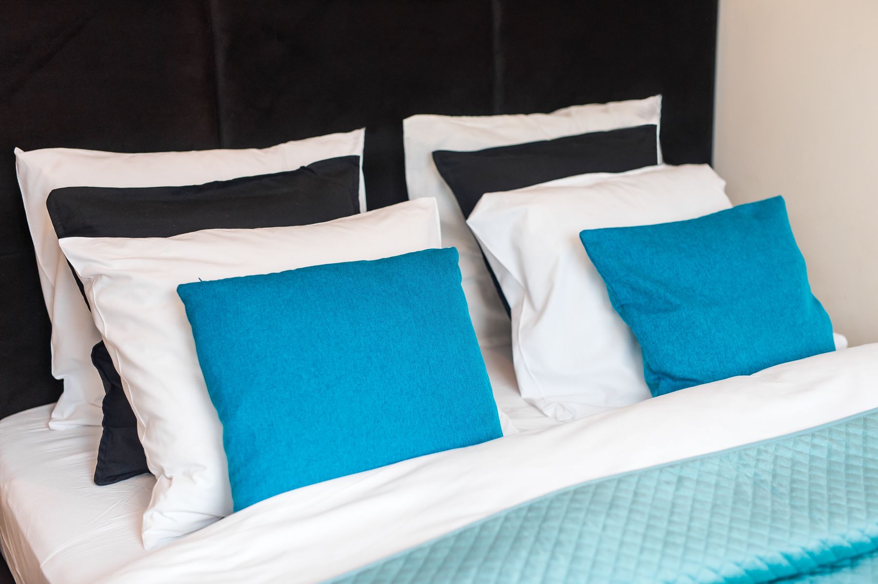 Una cama con almohadas blancas y azules, una colcha color turquesa y un cabecero negro.
