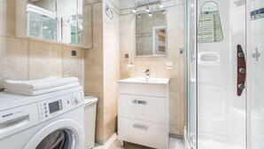 Ein modernes Badezimmer mit Waschmaschine, Duschkabine aus Glas und einem Waschtisch mit Spiegel.