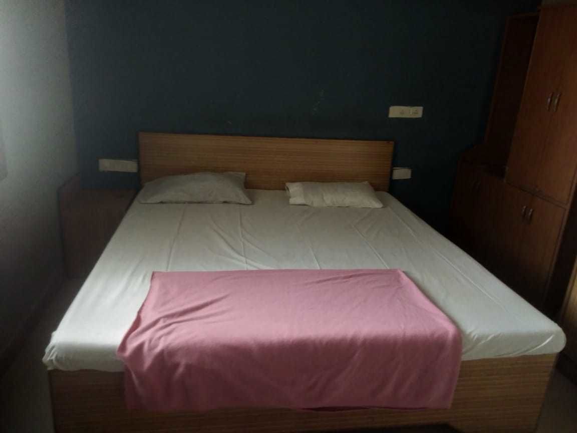 A single bed with a wooden headboard, two pillows, and a pink blanket.