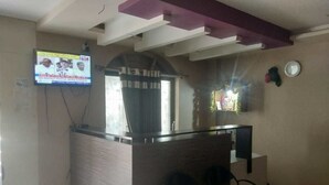 A reception area with a counter, a television mounted on the wall, and a window with curtains. - iROOMZ Pranathi Comforts (Ballari)