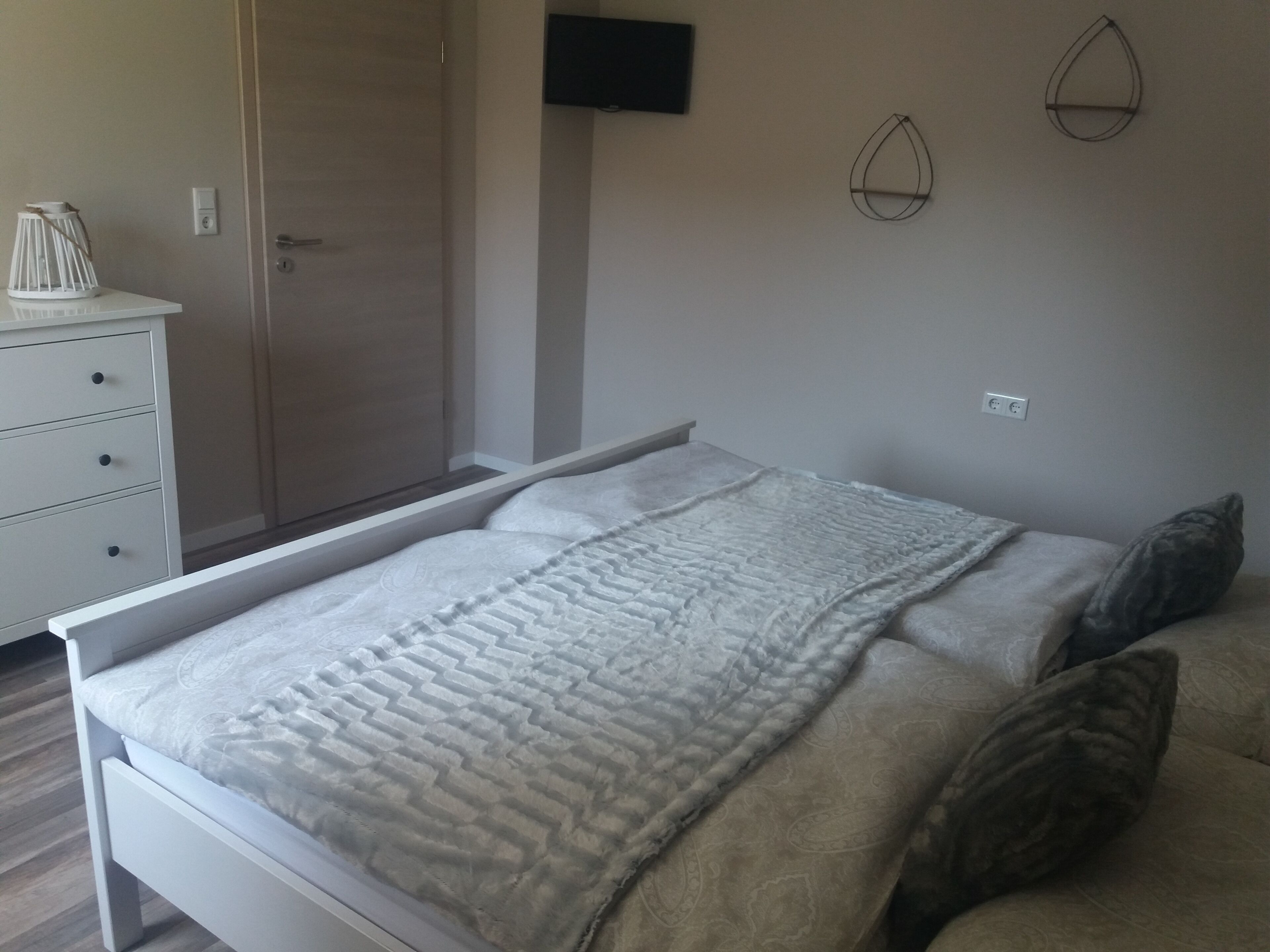 A bedroom with a bed, a wardrobe, a television, and a wall-mounted light fixture.