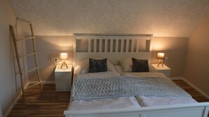 Een slaapkamer met een houten trap, twee nachtkastjes met lampen, een bed met hoofdeinde en behang met een patroon.
