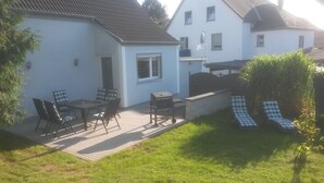 Een terras met een tafel, stoelen, een barbecue en twee loungestoelen.