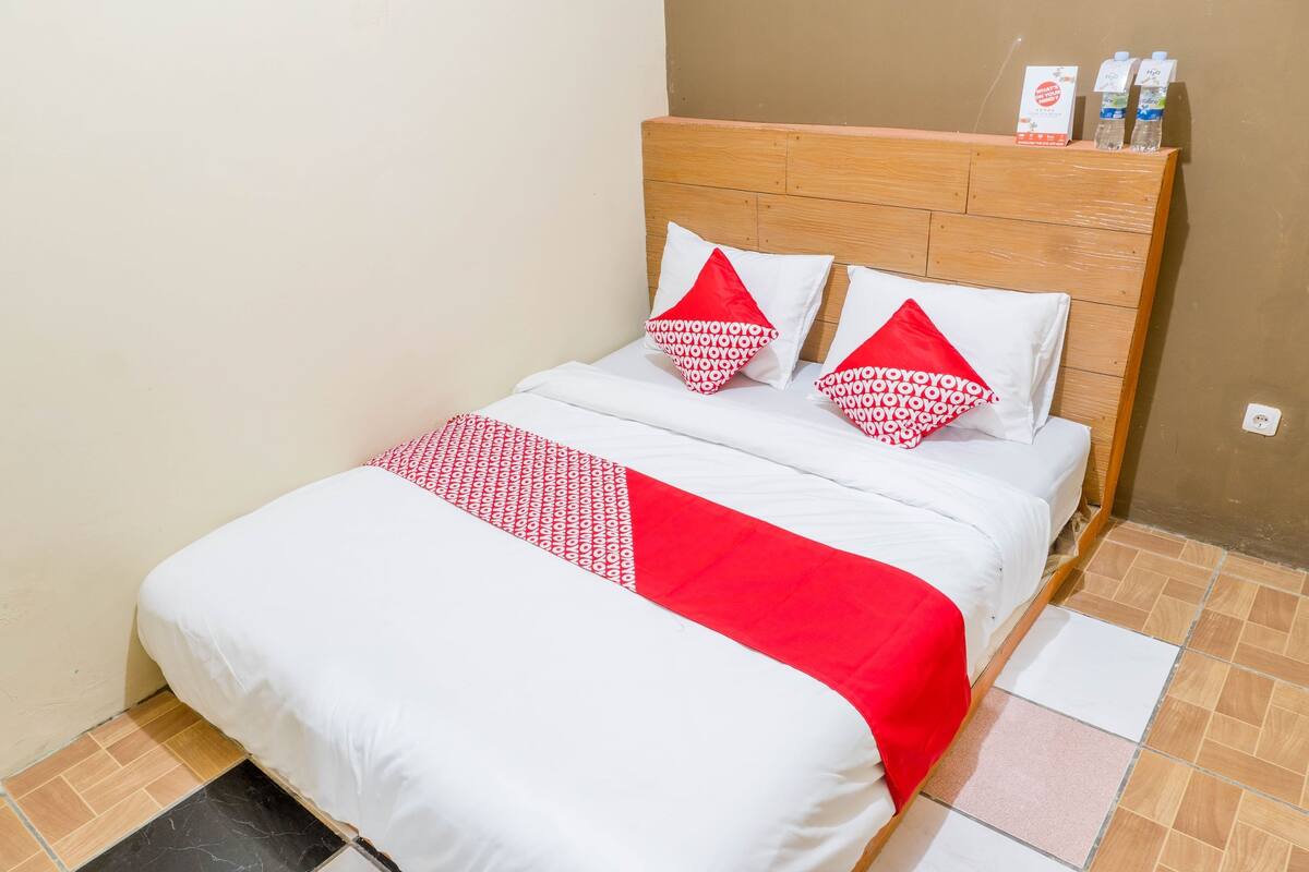 A neatly made bed with a wooden headboard, white and red bedding, and two pillows with a red and white pattern.