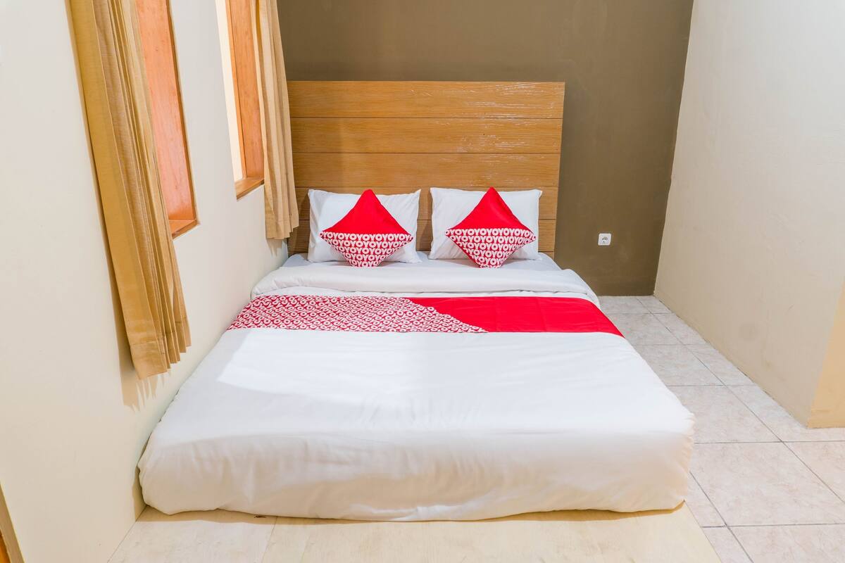 A neatly made bed with white and red bedding, a wooden headboard, and a small window with curtains.