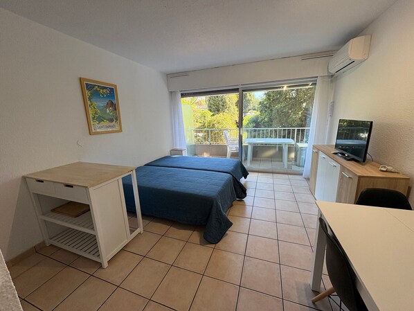 Une petite chambre propre, avec deux lits, un bureau, une télévision et un balcon donnant sur la verdure.
