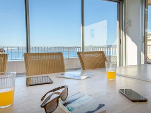 Enjoy the ocean view from this balcony with a table and wicker chairs.