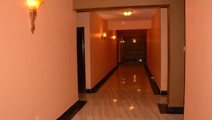 A corridor with a polished floor, a wall-mounted light fixture, and a door at the end. - Eden Hotel Emali (Emali)