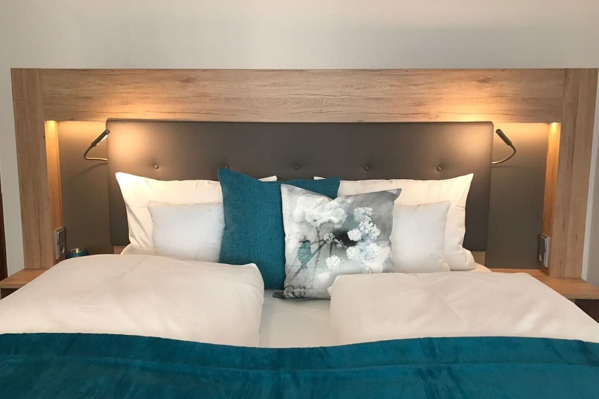 A bed with a wooden headboard, white and teal pillows, and a teal bedspread.