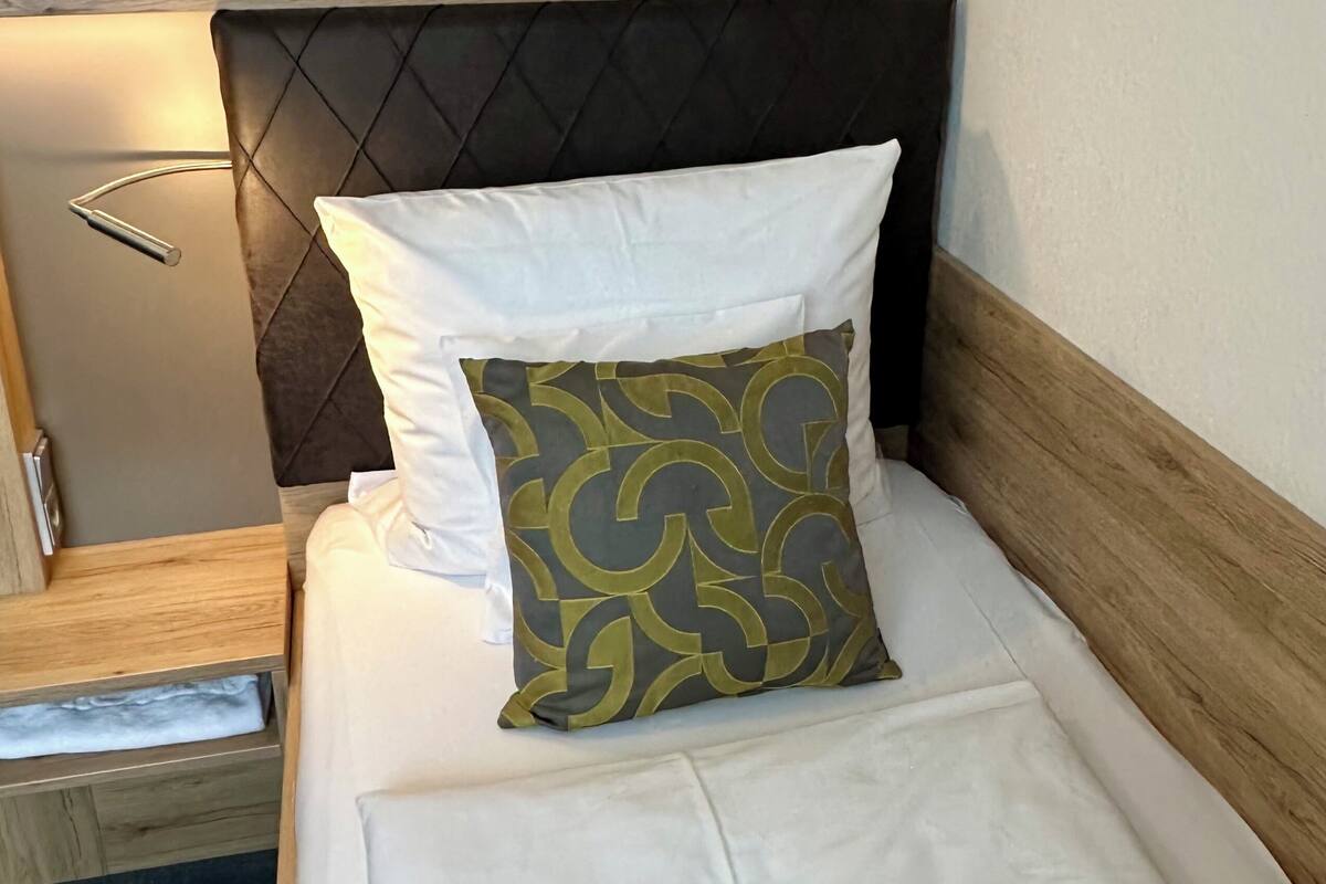 A bed with a wooden headboard, white bedding, and a patterned pillow.