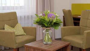 A room with two green armchairs, a small wooden table, and a vase with flowers. - Hotel Kronprinz (Kulmbach)