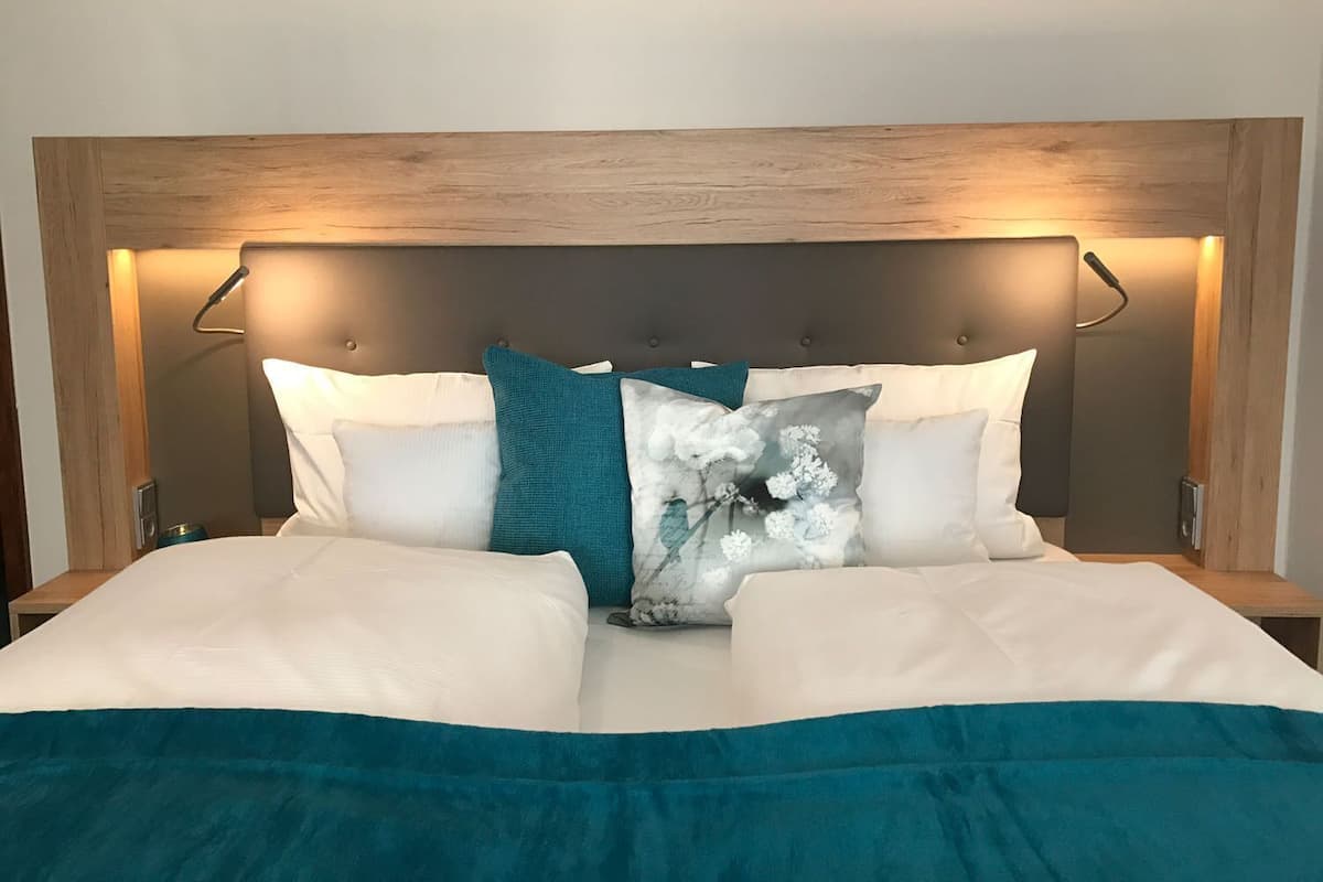 A neatly made bed with a headboard, multiple pillows, and a teal throw blanket.