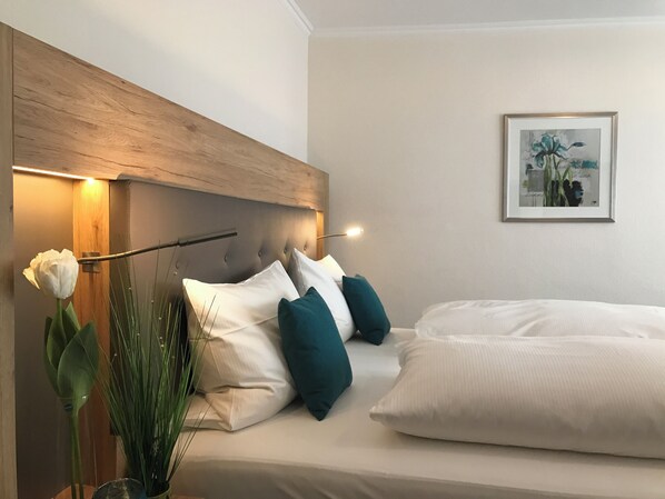 Una cama bien hecha con almohadas blancas y azul turquesa, un cabecero de madera y un cuadro colgado en la pared.