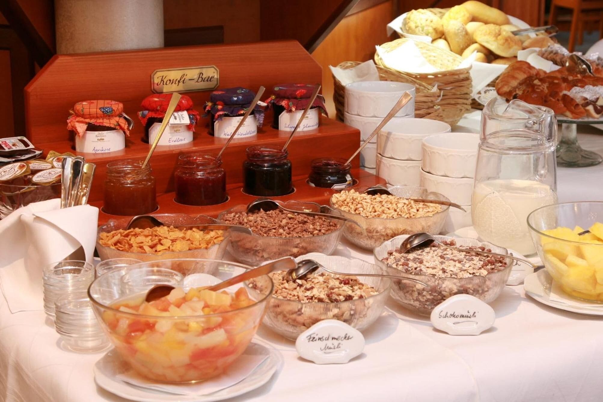 A buffet with various food items and condiments, including jars of preserves and bowls of cereal and fruit.
