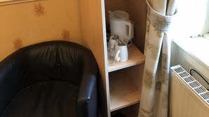 Huoneessa on musta nahkainen tuoli, valkoinen patteri ja hylly, jonka päällä on vedenkeitin ja kuppeja.