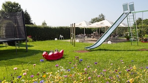 A playground with a slide and swings, surrounded by a grassy area with colorful flowers. - Venngasthof Zur Buche (Monschau)