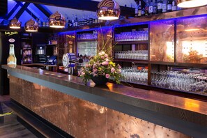 Eine Bar mit einer Kupfer-Theke, Regalen für Gläser und einer floralen Dekoration.