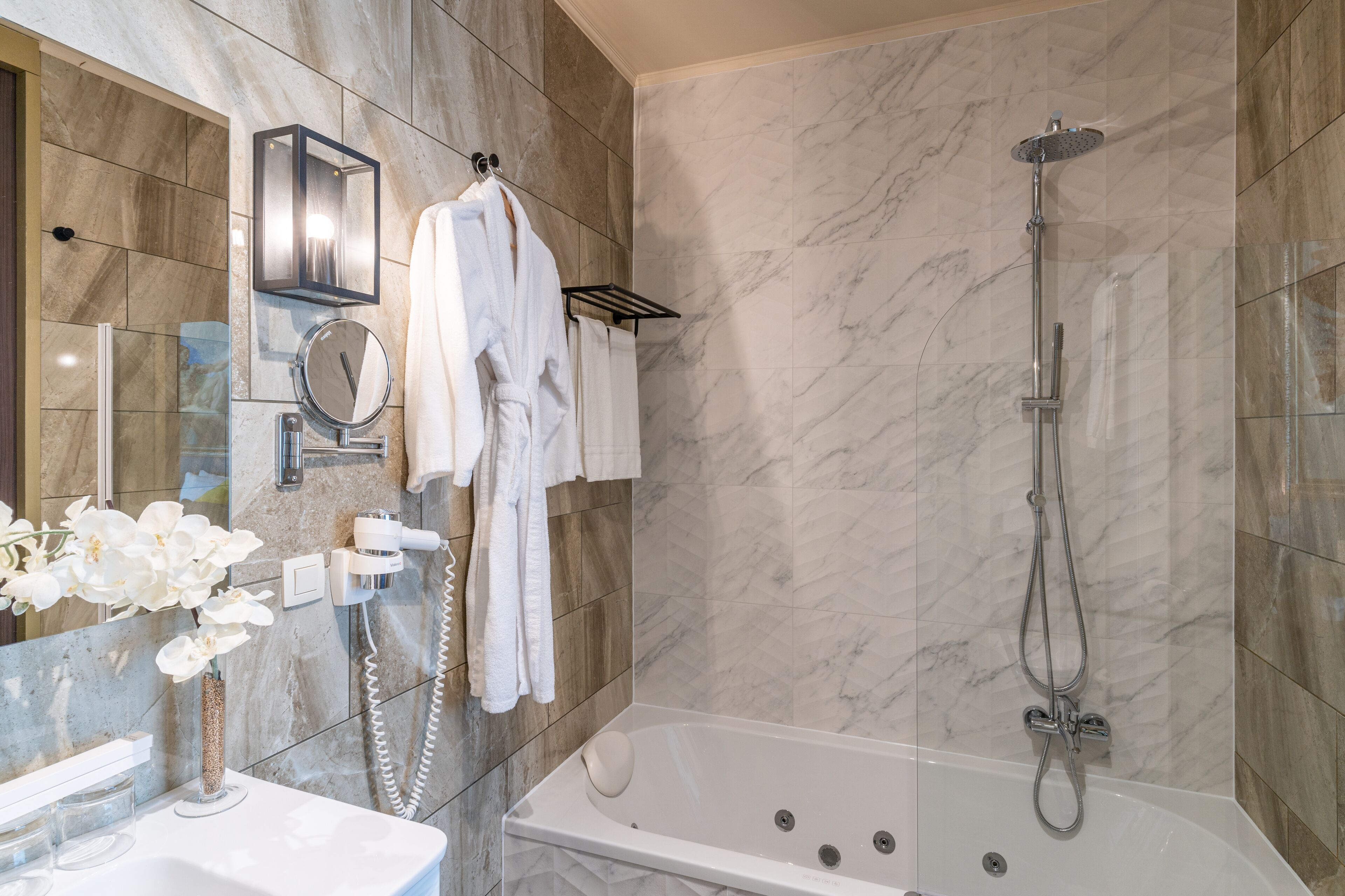 Une salle de bain moderne avec un mur en marbre, une baignoire, une douche, un meuble-lavabo avec un miroir et un porte-serviettes.