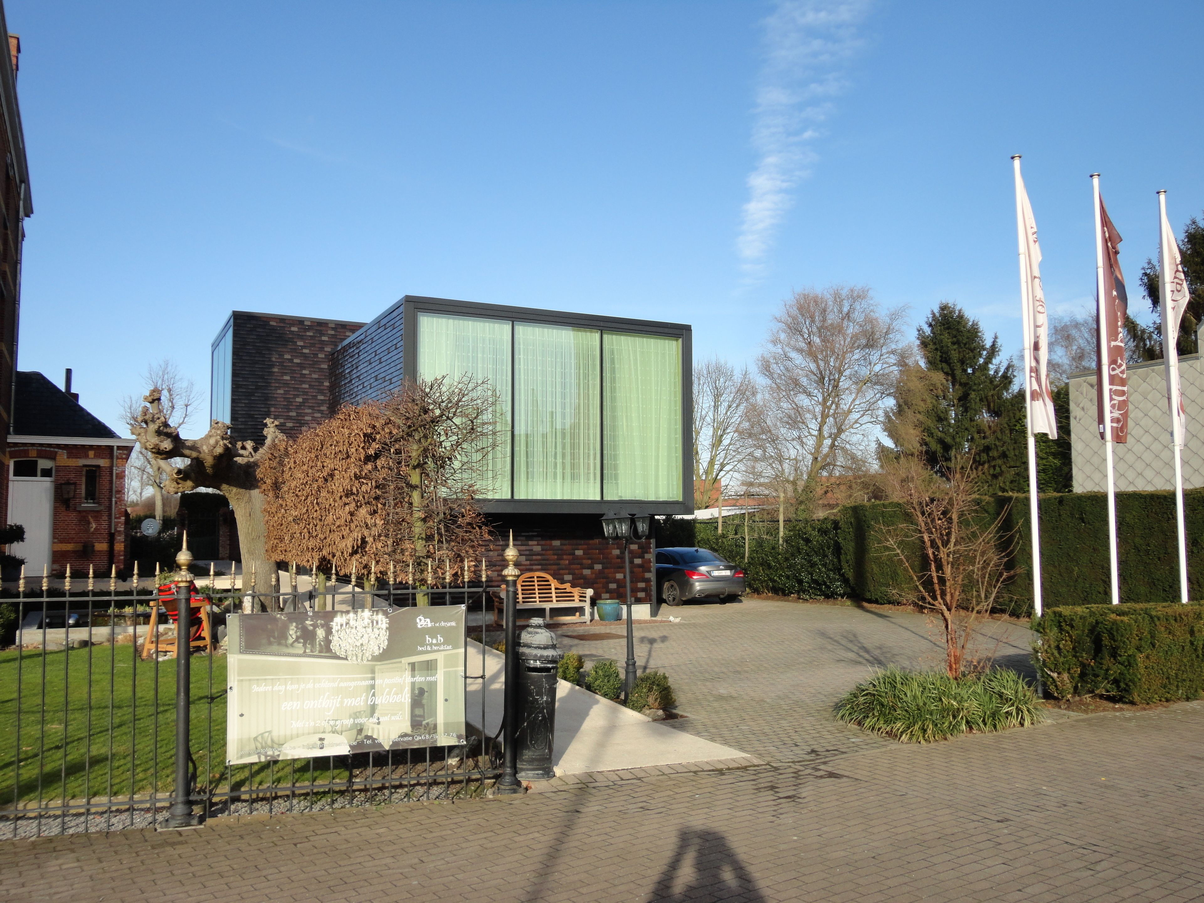 Un edificio moderno con ampie vetrate, vialetto lastricato e un'auto parcheggiata di fronte.