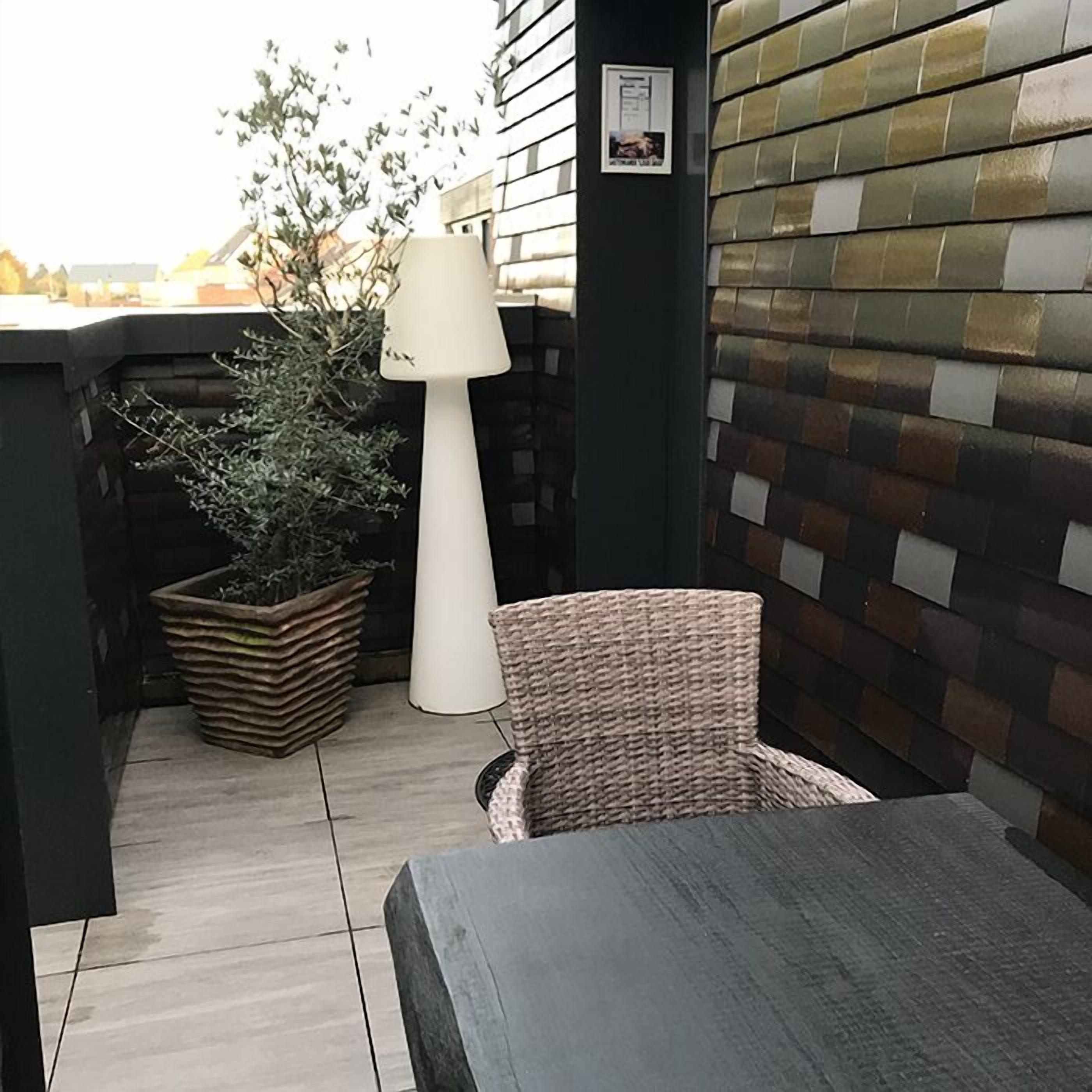 A patio area with a wicker chair, a table, a potted plant, and a lamp.