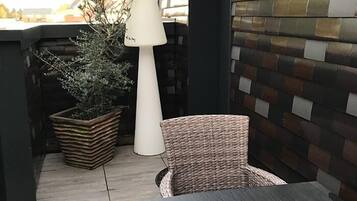 A patio area with a wicker chair, a table, a potted plant, and a lamp.