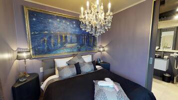 Een slaapkamer met een groot schilderij van een nachtelijke scène, een kroonluchter en een moderne badkamer die door een open deur zichtbaar is.