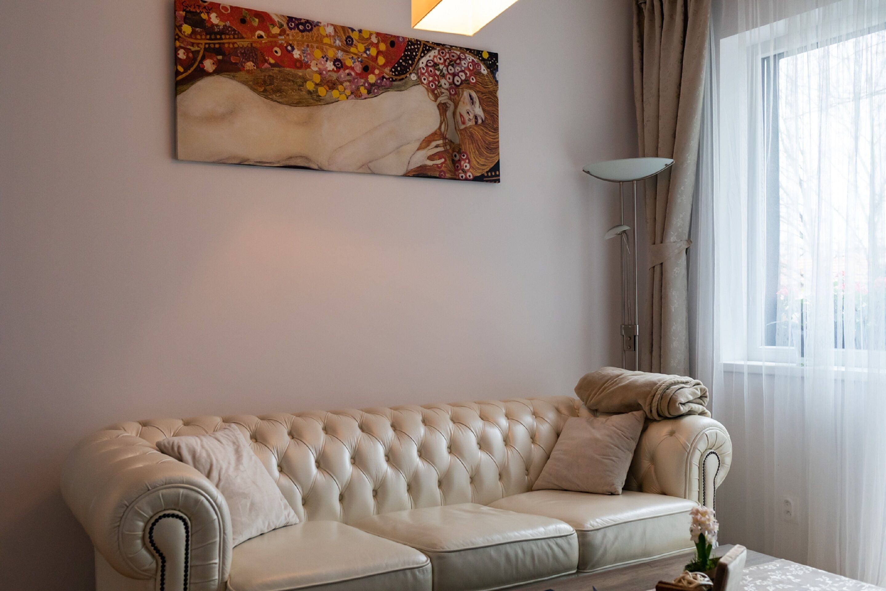 Ett modernt vardagsrum med en beige lädersoffa, en stor abstrakt målning och en golvlampa.