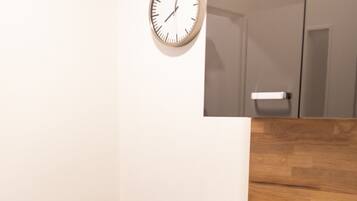 Un rincón de una habitación con un escritorio de madera, una silla gris, un reloj de pared y un armario.