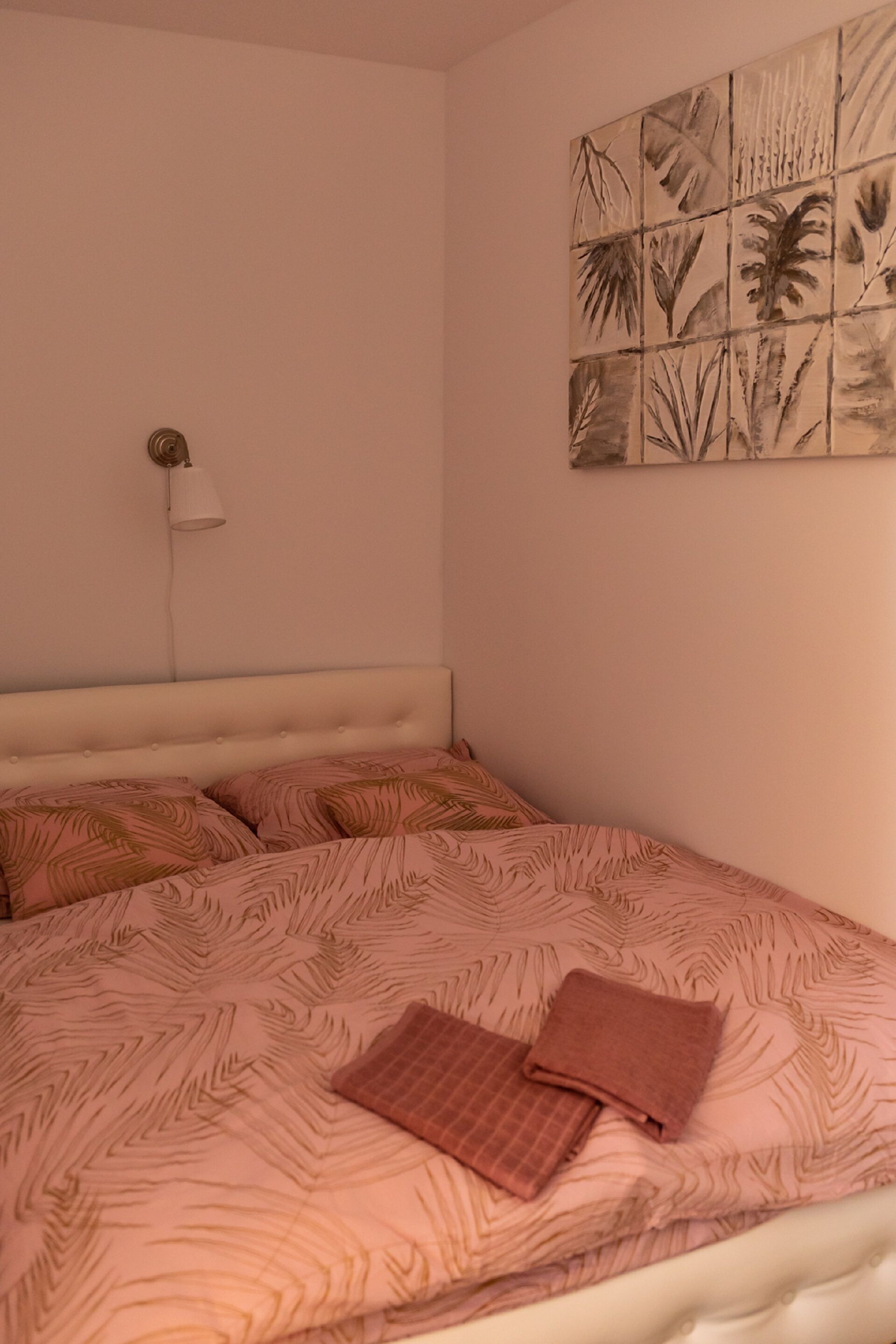 A bedroom with a bed, a wall-mounted light, and a wall art piece.