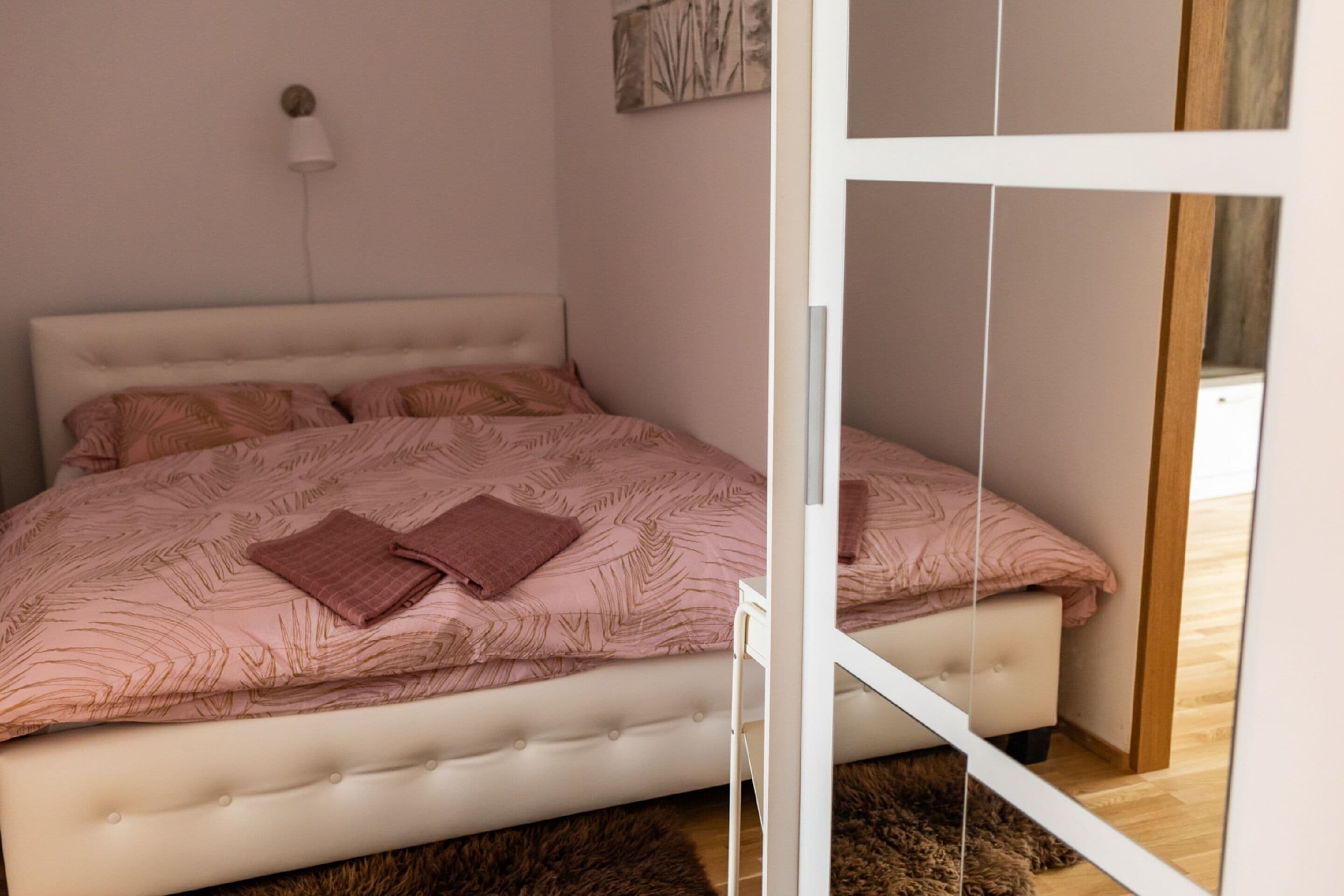 Een slaapkamer met een bed, een wandlamp en een deur.