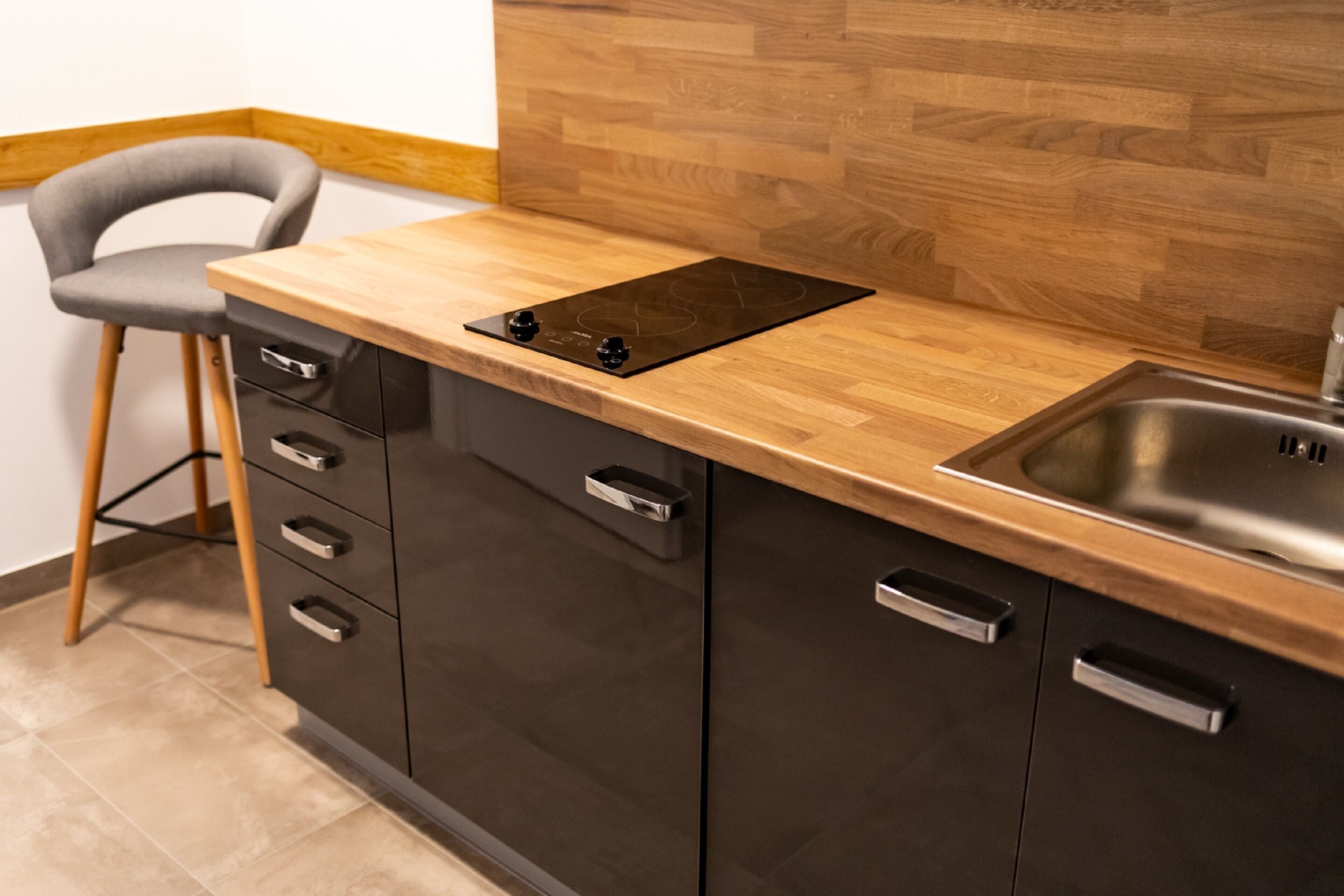 A modern kitchen with a wooden countertop, a built-in stove, a sink, and a chair.