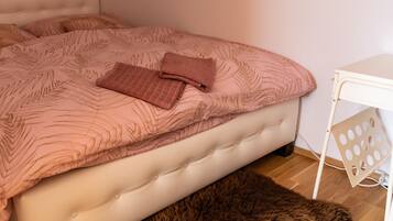 Une chambre à coucher avec une tête de lit capitonnée, une couvre-lit à motifs, un coussin décoratif plié, un tapis moelleux et une table de chevet blanche au motif ajouré.