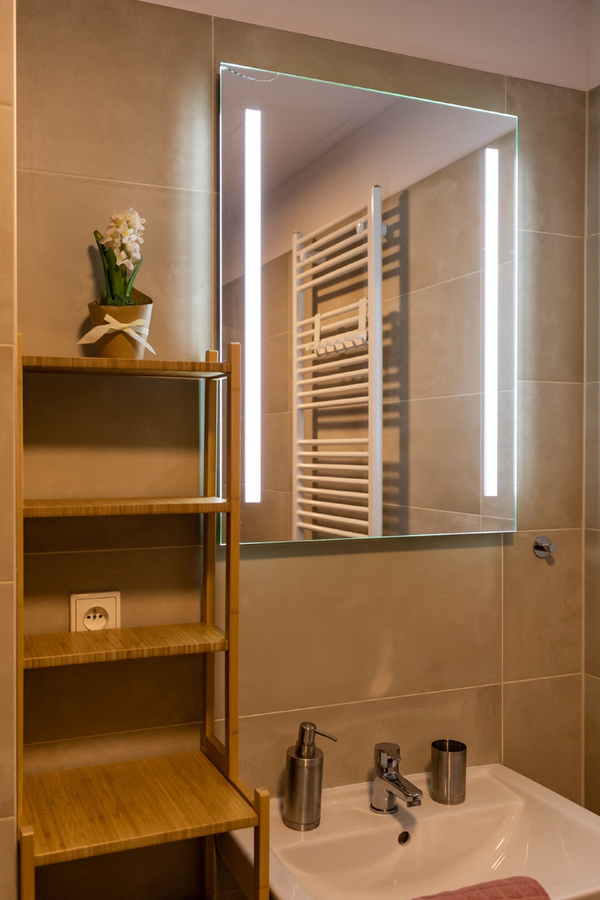 A bathroom with a white sink, a mirror, and a wooden shelf with a vase of flowers.