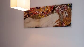 Un sofá color beige con textura, un cojín decorativo, una mesita con un florero y una obra de arte colgada en la pared.