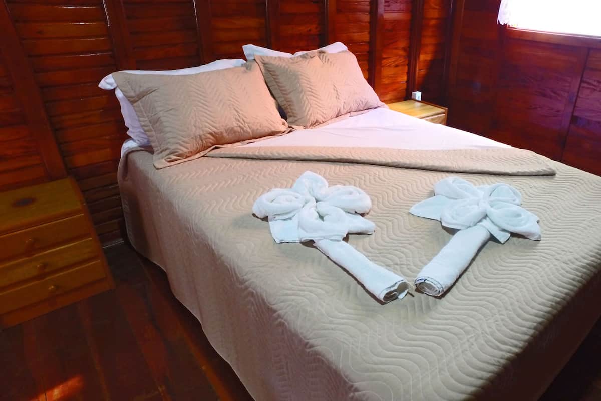 A neatly made bed with a beige quilt, two pillows, and two towels arranged on the bed.