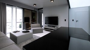 A modern living room with a large flat-screen TV, grey sofas, and a large window providing a view of the outside. - Super-Apartamenty - Andersia VIP (Poznan)