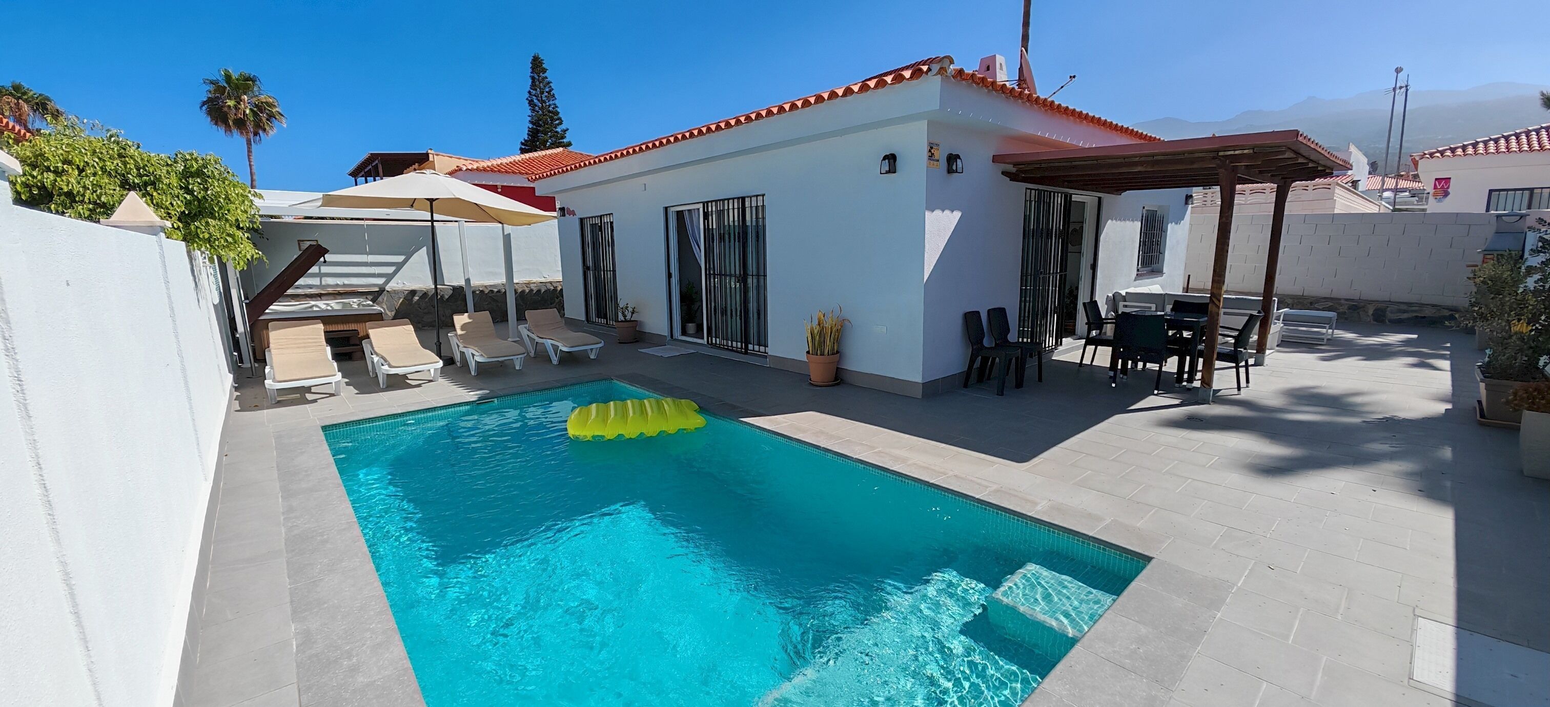 A swimming pool with lounge chairs, a pergola, and a covered patio area.