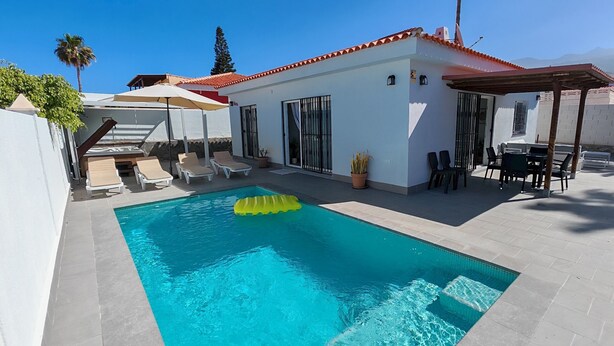 En pool med solstolar, en pergola och en täckt uteplats.