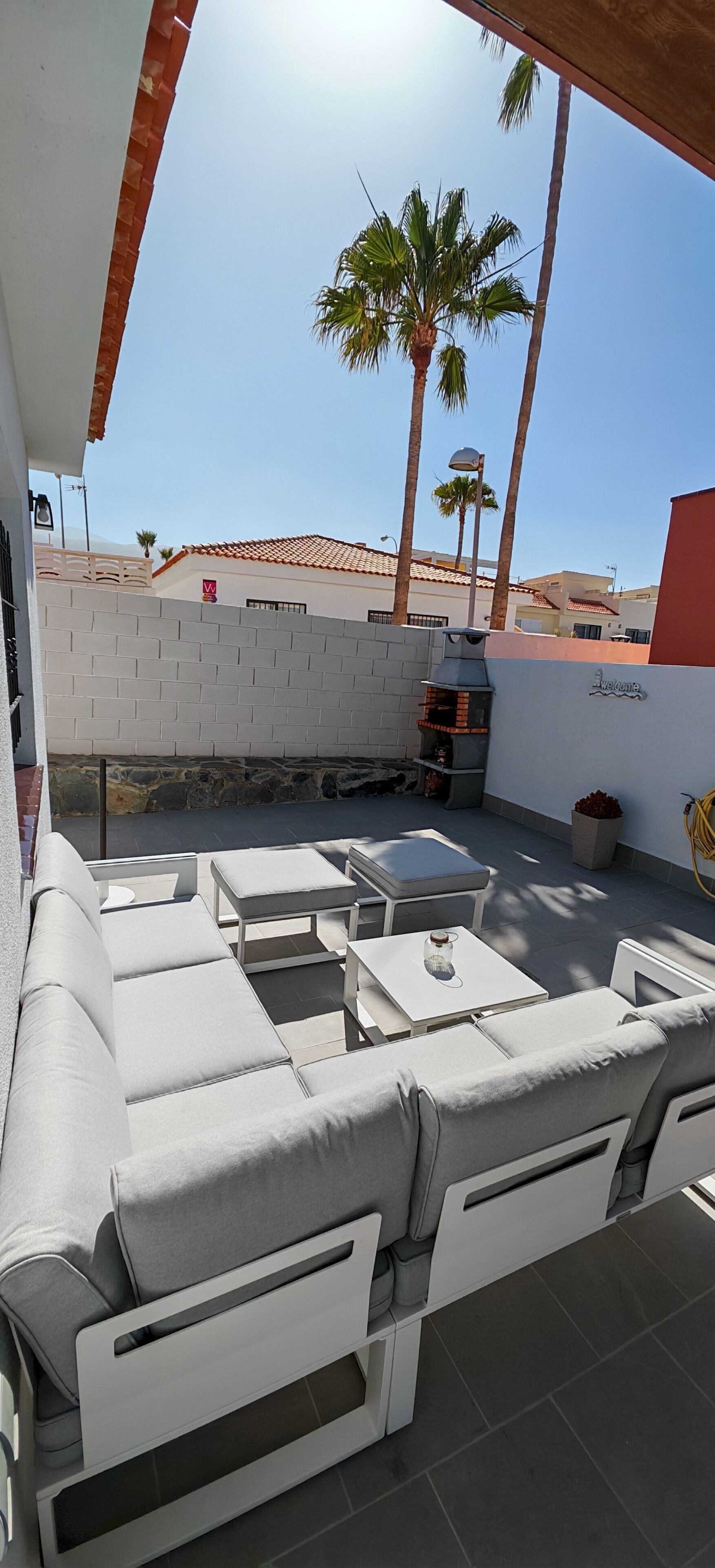An outdoor patio with white cushioned seating, a small table, and a barbecue grill.